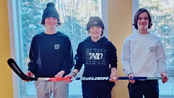 Two boys in NoahStrong hoodies holding a hockey stick